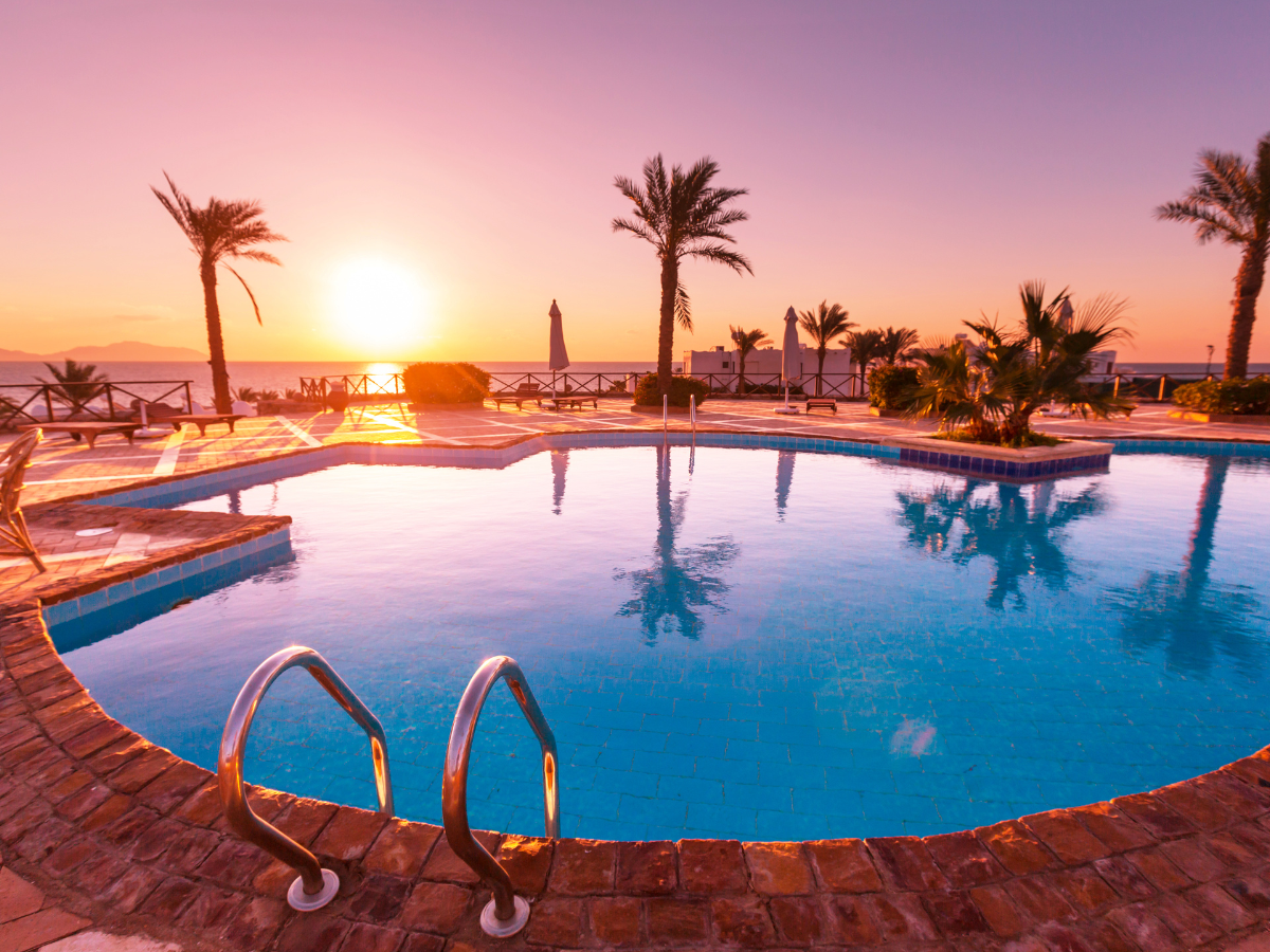 Swimming pool with palm trees at sunset. Water reflects the warm colors of the sky.