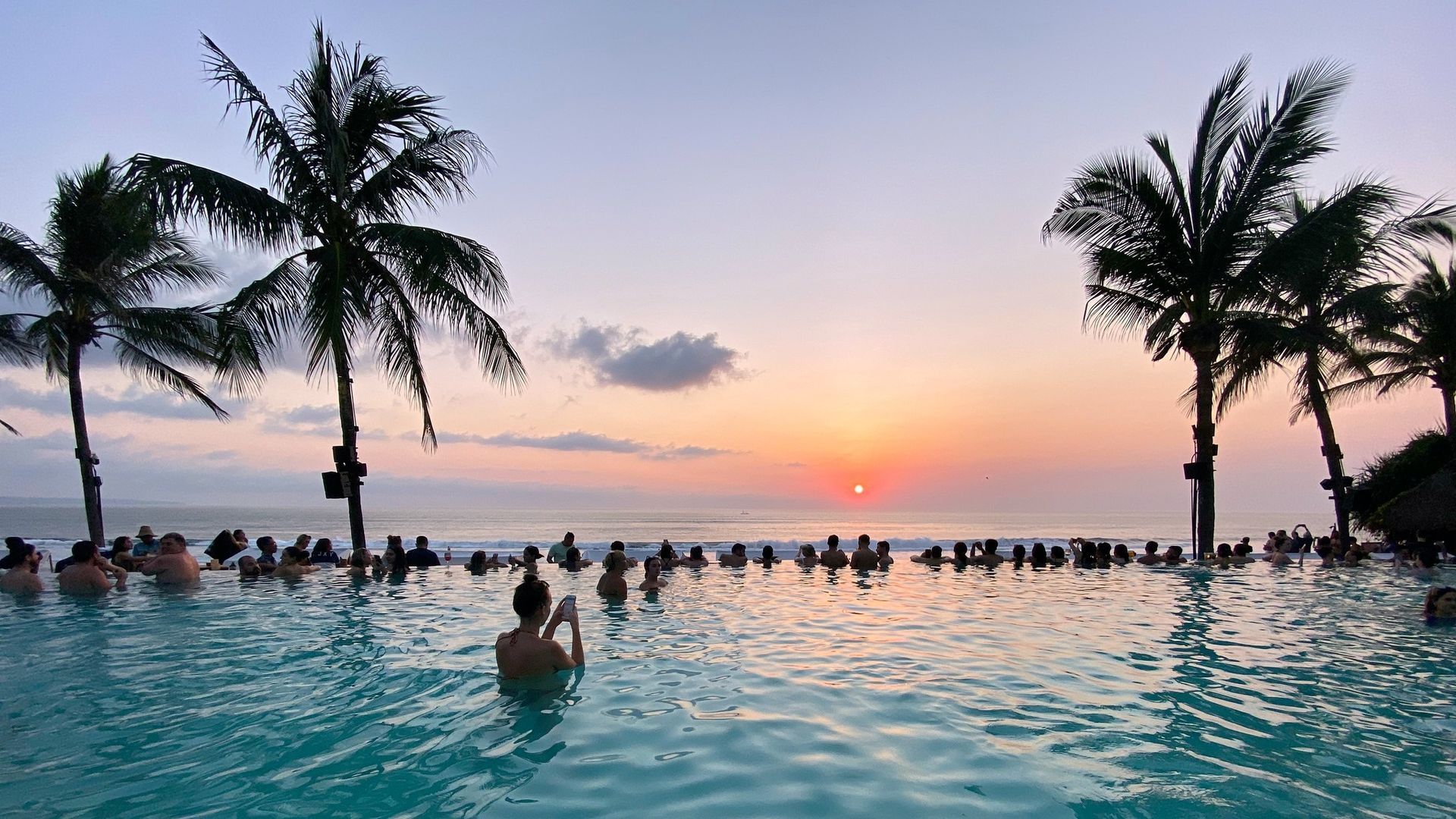 A group of people are swimming in an infinity pool at sunset.