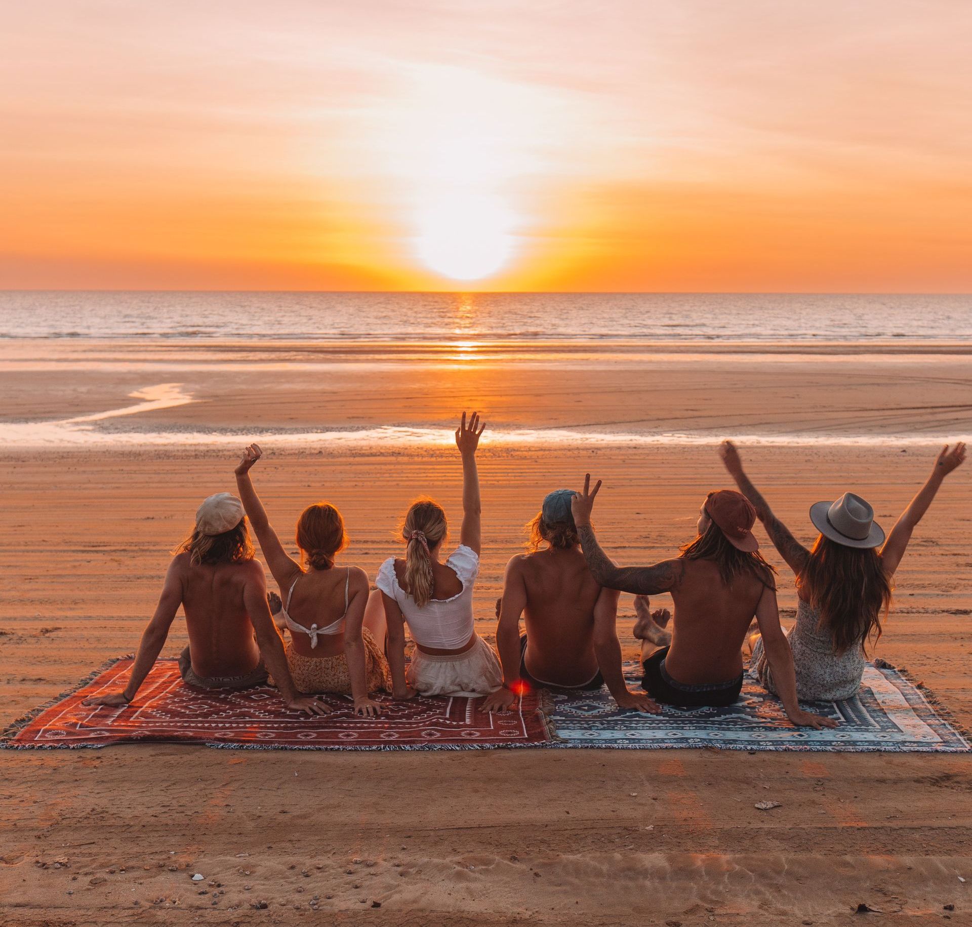 A group of people are sitting on a blanket on the beach at sunset.