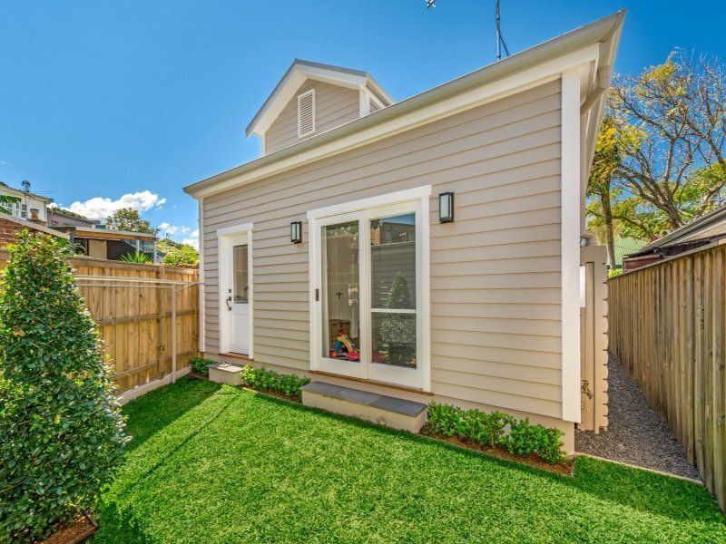 A small house with a fence and a lawn in front of it.