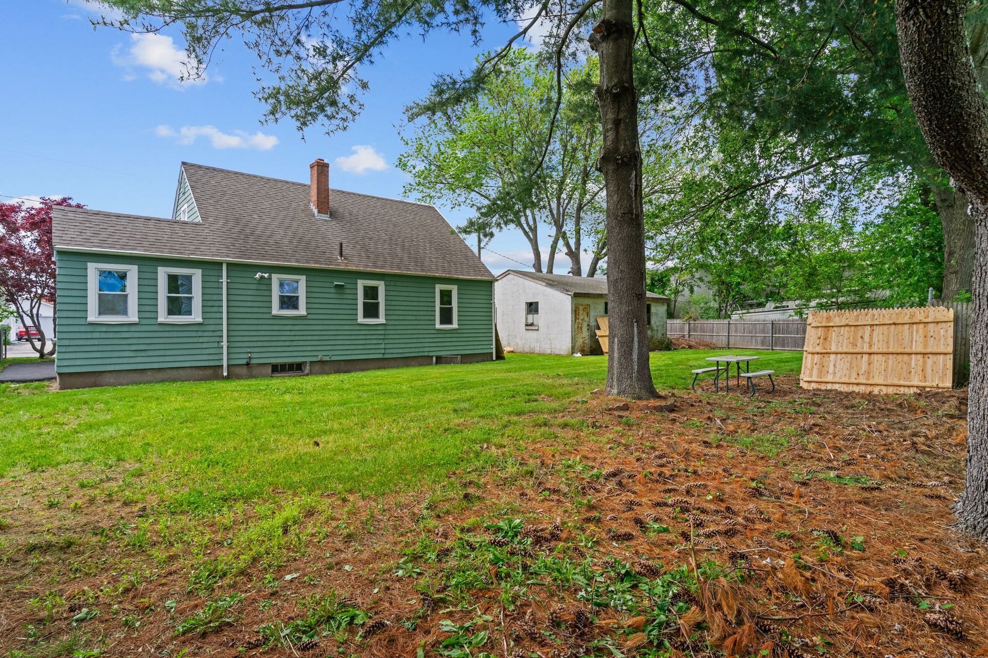 A green house is sitting in the middle of a lush green yard.