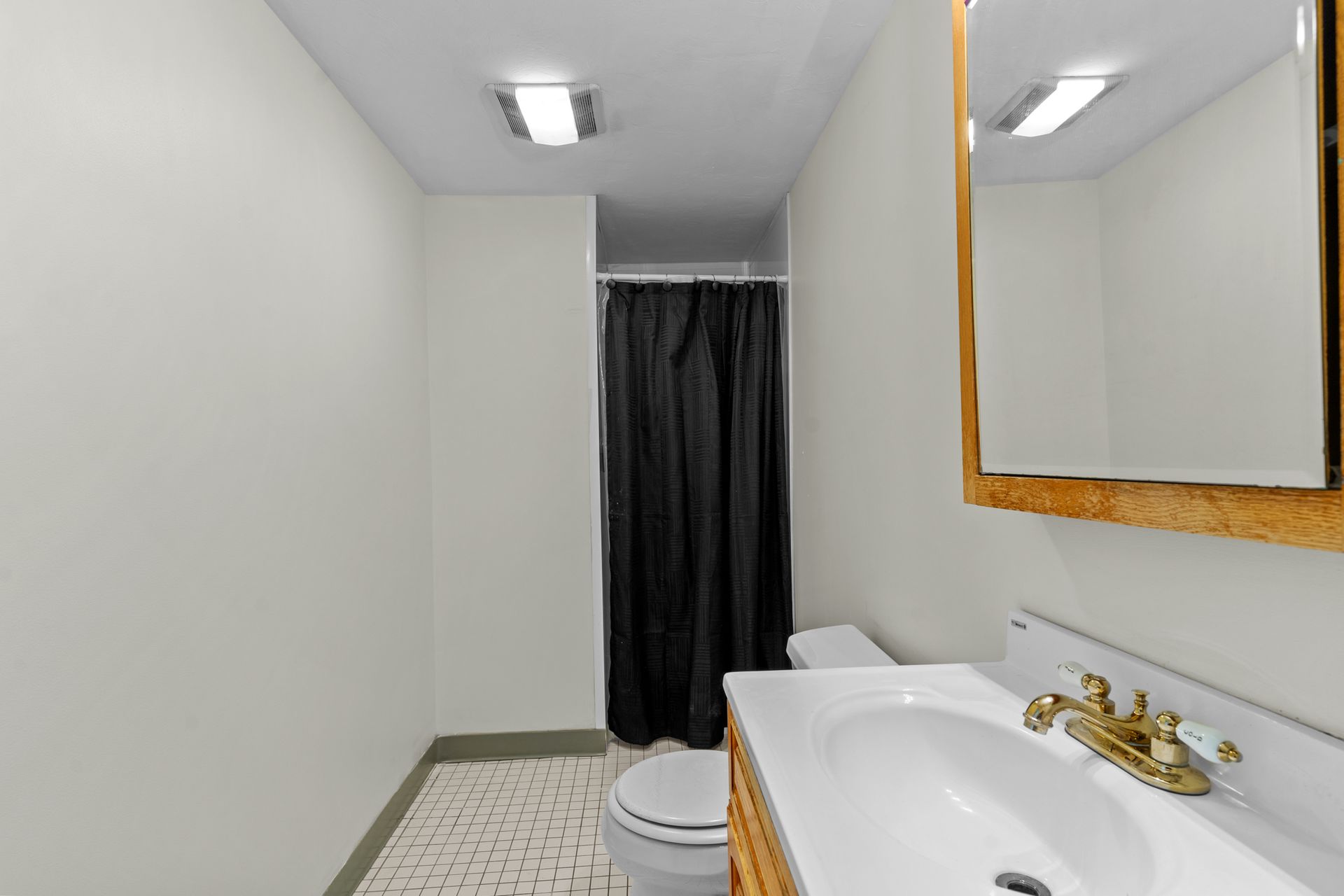 A bathroom with a toilet, sink, mirror and shower curtain.