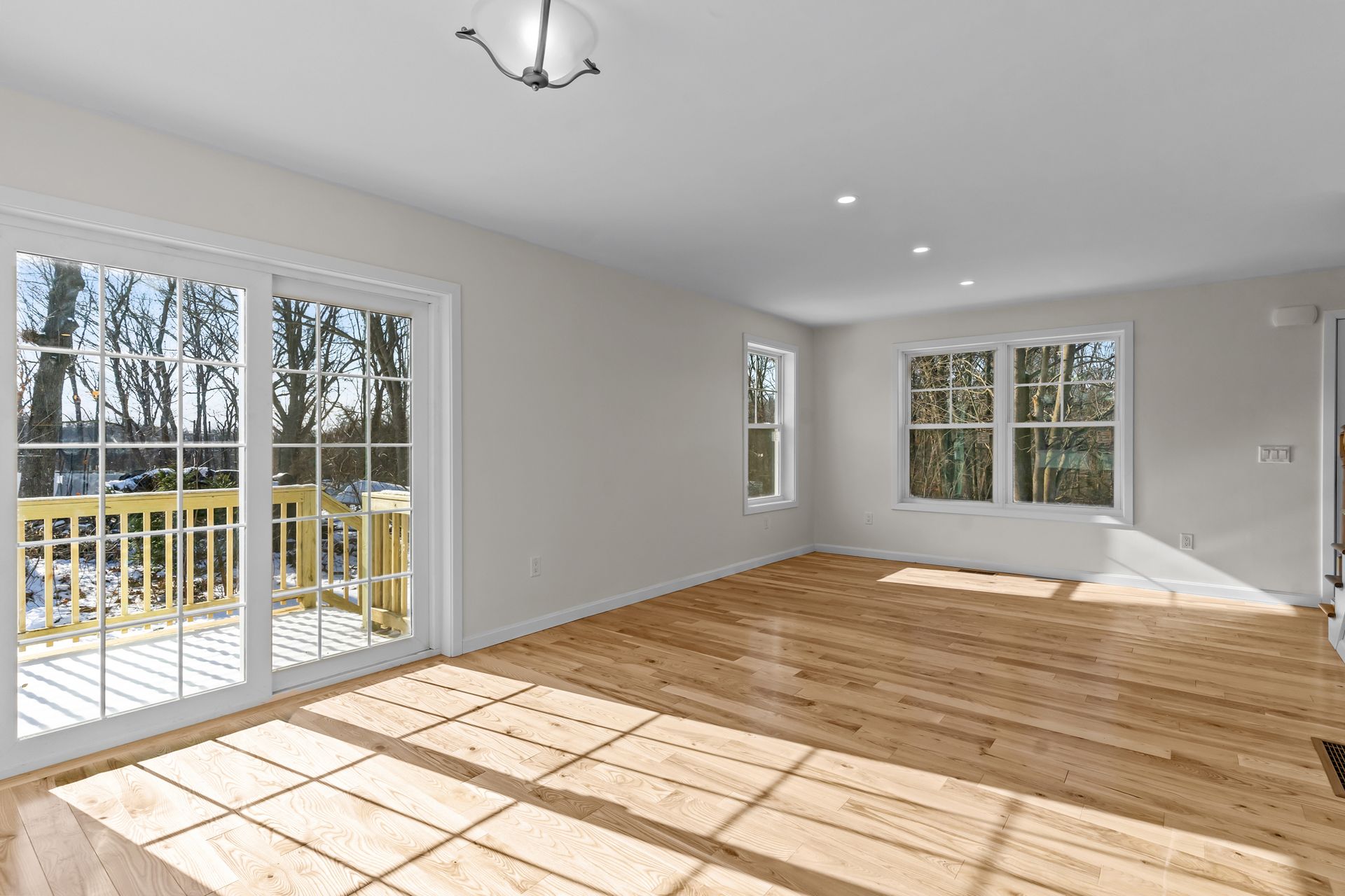 An empty living room with hardwood floors and sliding glass doors leading to a deck.