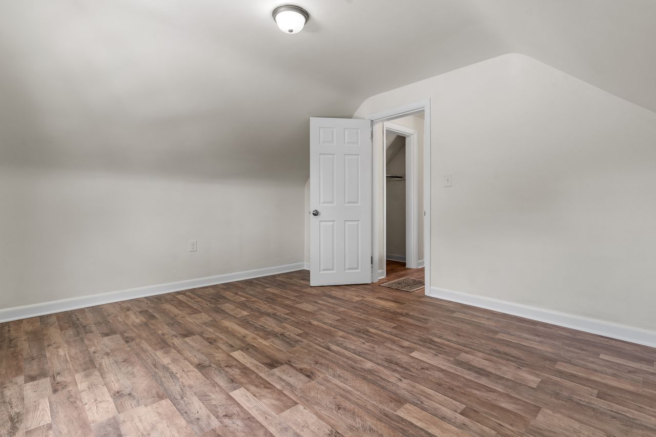 An empty bedroom with hardwood floors and white walls.