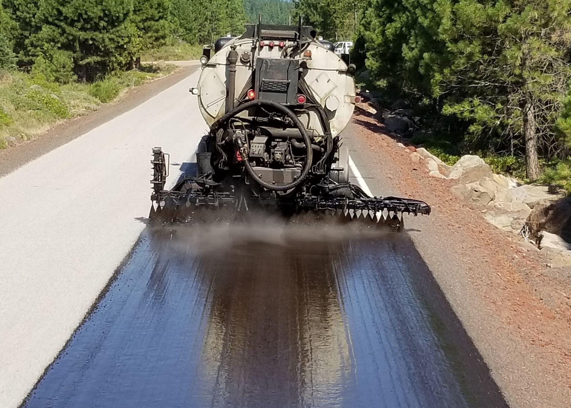 A truck is spraying sealcoat on asphalt.