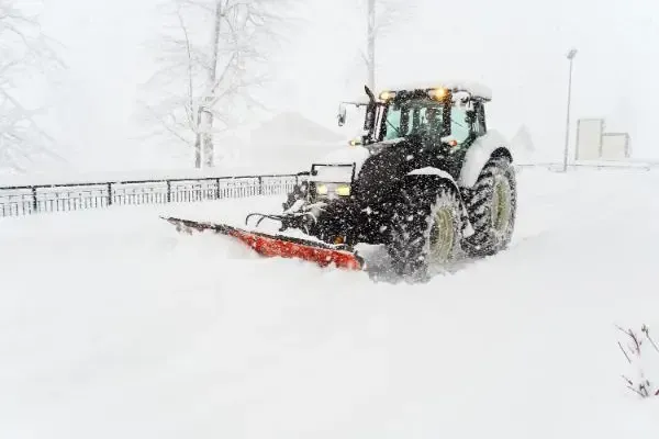 A tractor is plowing snow on a snowy commercial parking lot.