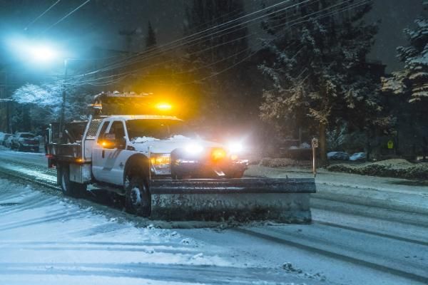 A snow plow is clearing snow from a parking at night.