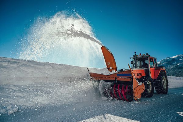 A snow blower is blowing snow from a parking lot.