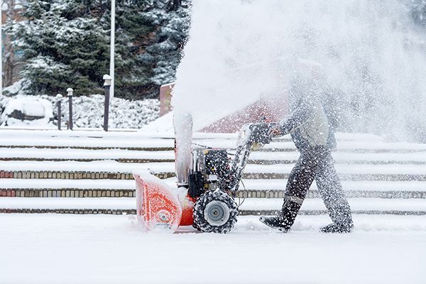 A man is using a snow blower to clear snow from a sidewalk.