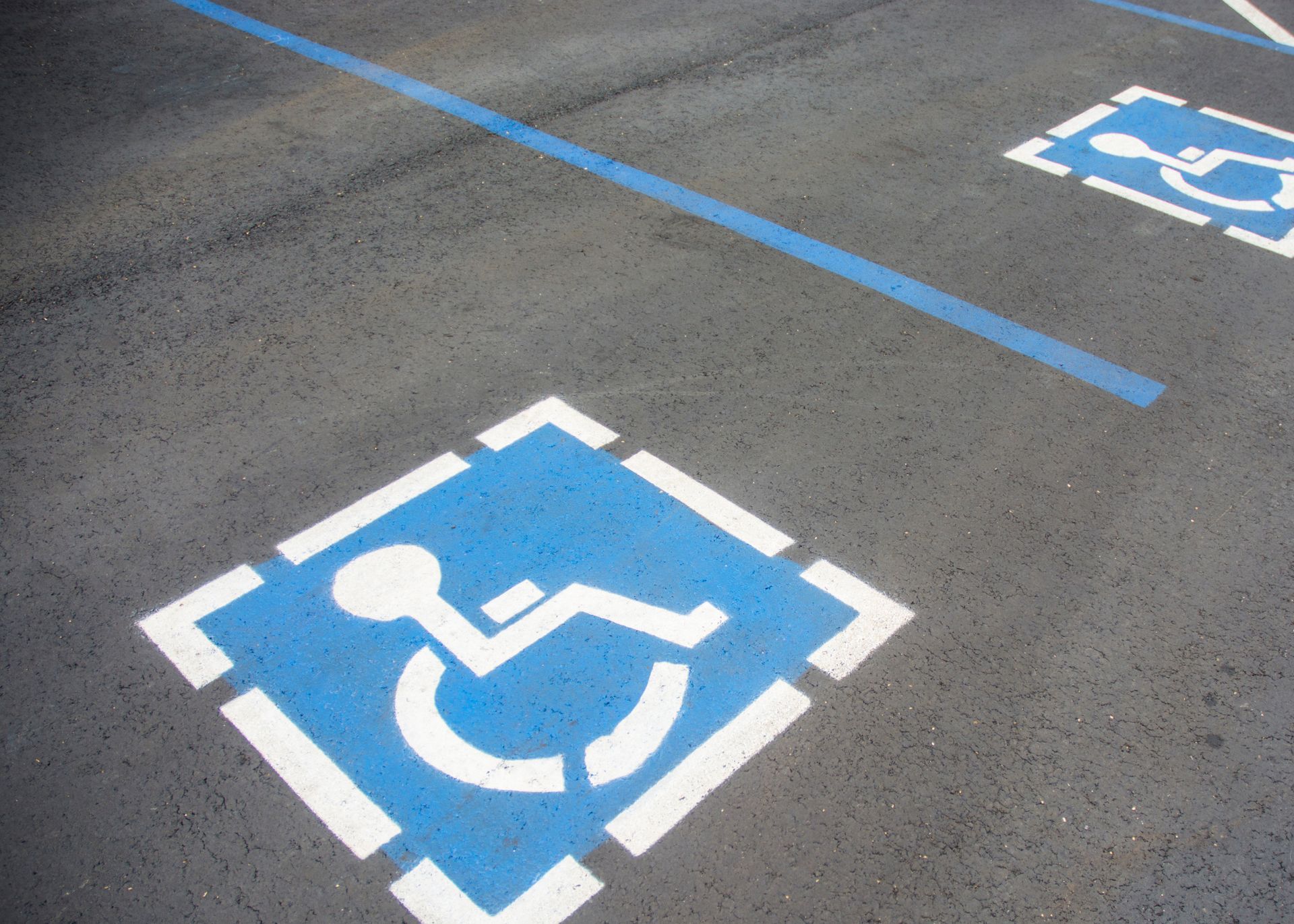 A blue and white handicapped sign is painted on an asphalt parking lot.