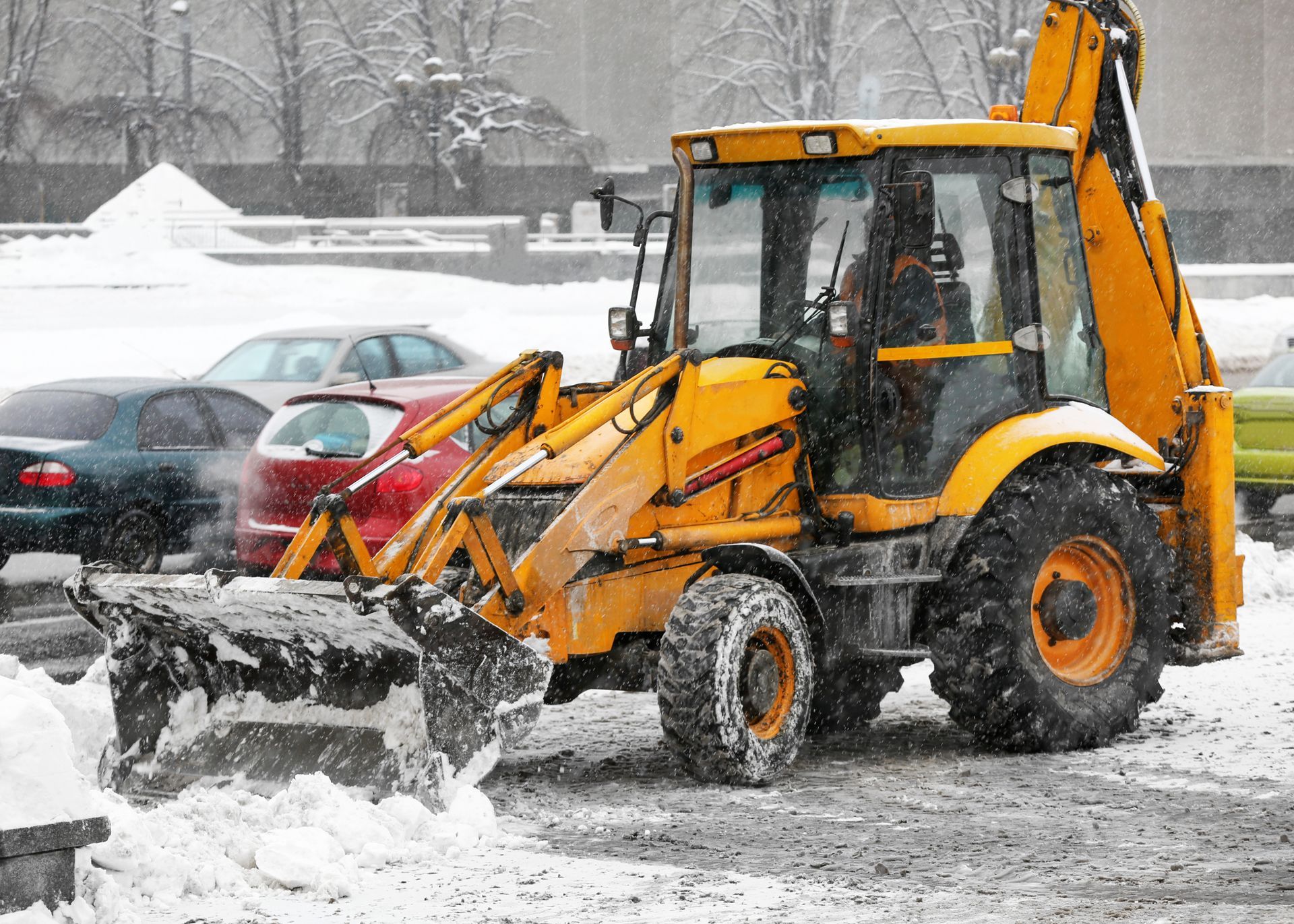 A yellow tractor is clearing snow from a parking lot.