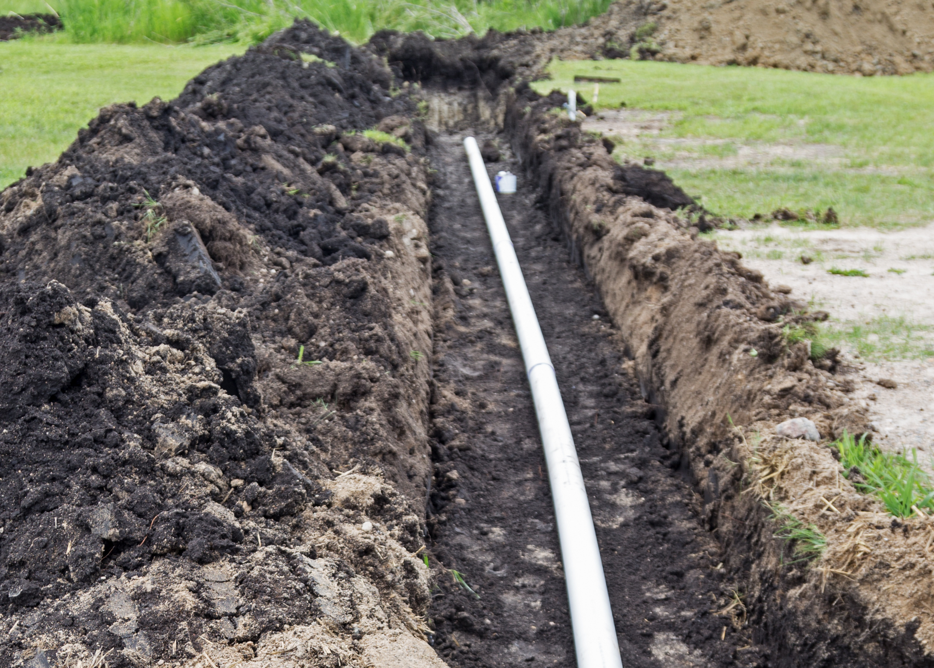 A drainage pipe is being installed in a trench in the dirt.