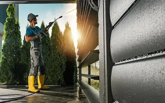 A man is cleaning an exterior wall with a heated power washer.
