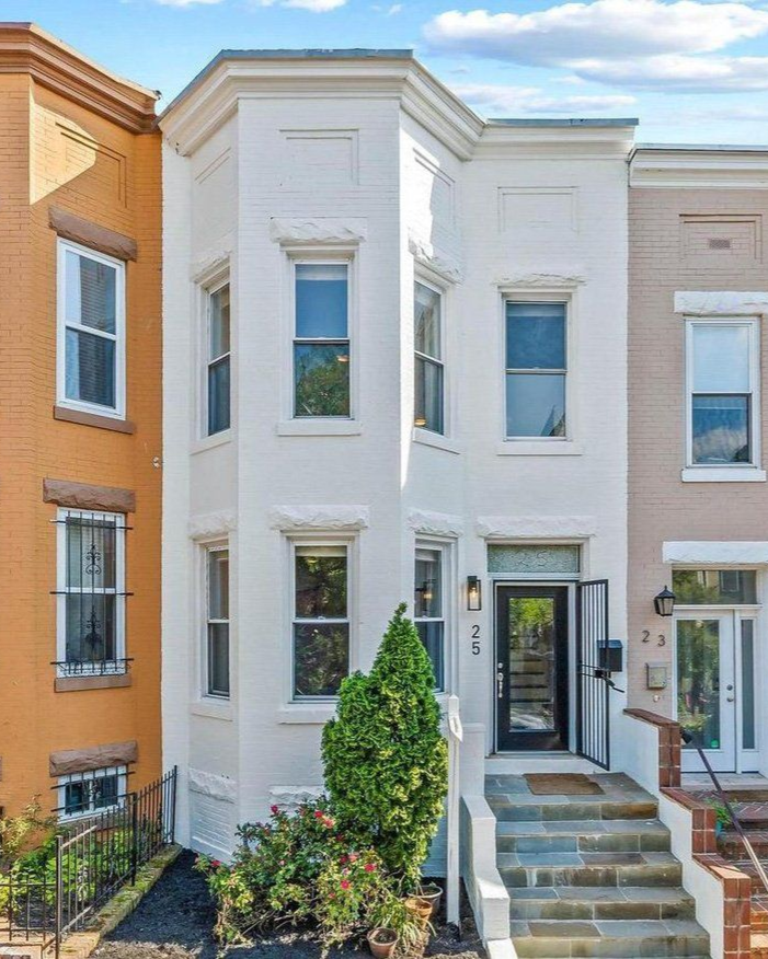 Three Washington DC rowhomes connected together one is light orange one is white and one is creme each have eight windows