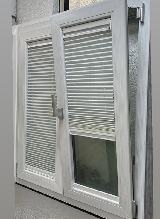 Finestre a doppio vetro bianche, parzialmente aperte con tende integrate che coprono la parte superiore.