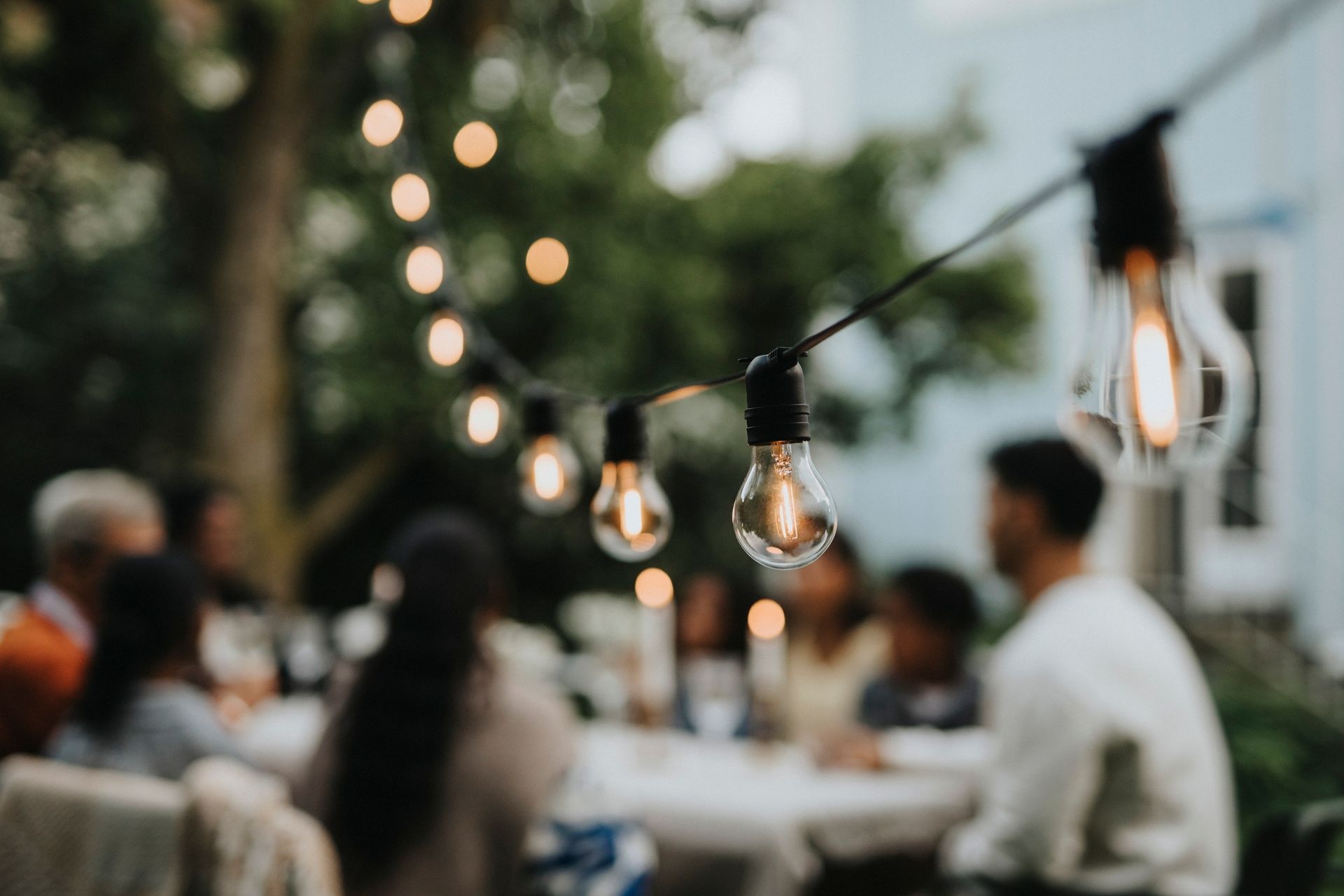 Illuminated string lights hanging in garden during party, showcasing outdoor lighting services. Illuminated string lights hanging in garden during party, showcasing outdoor lighting services.