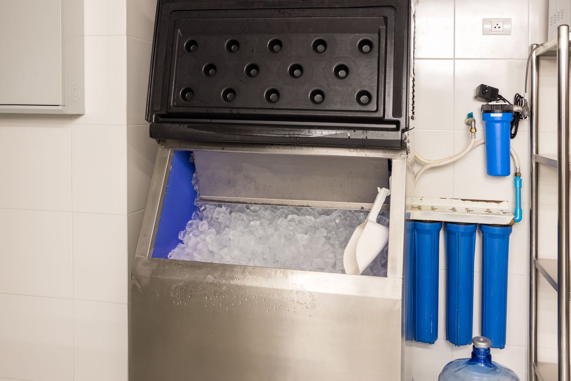A stainless steel ice machine is filled with ice in a kitchen.