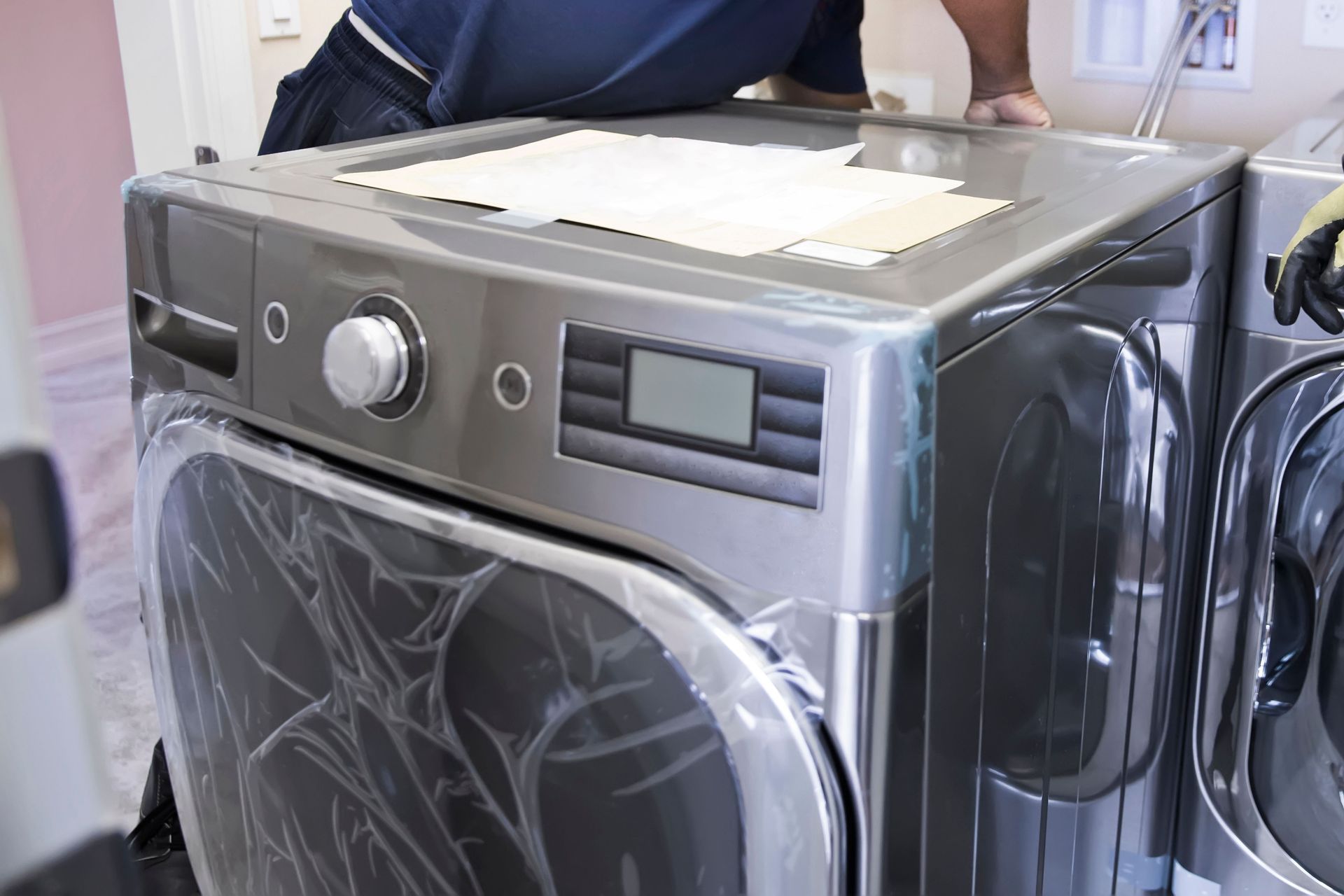 A man is standing next to a washing machine and dryer in a laundry room.
