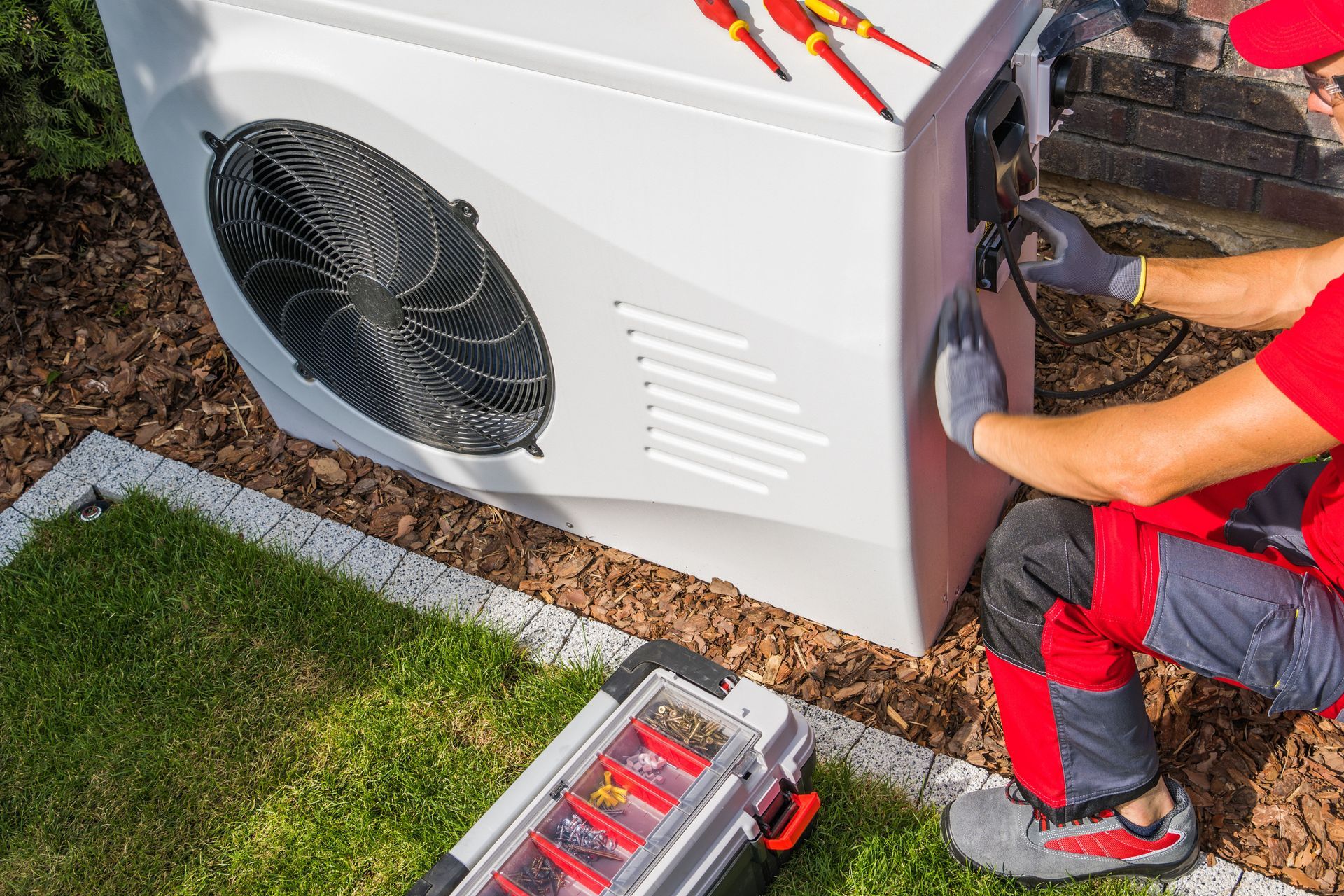 A man is working on a heat pump in a backyard.