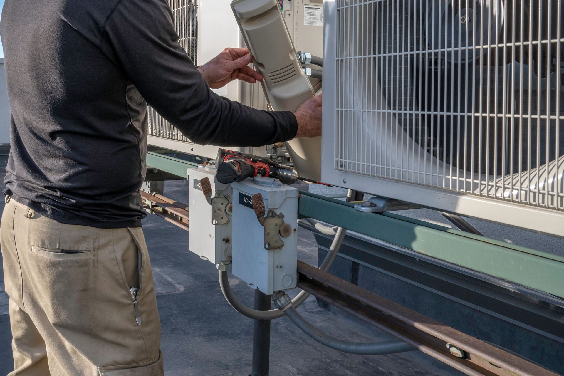 A man is working on an air conditioner on top of a building.