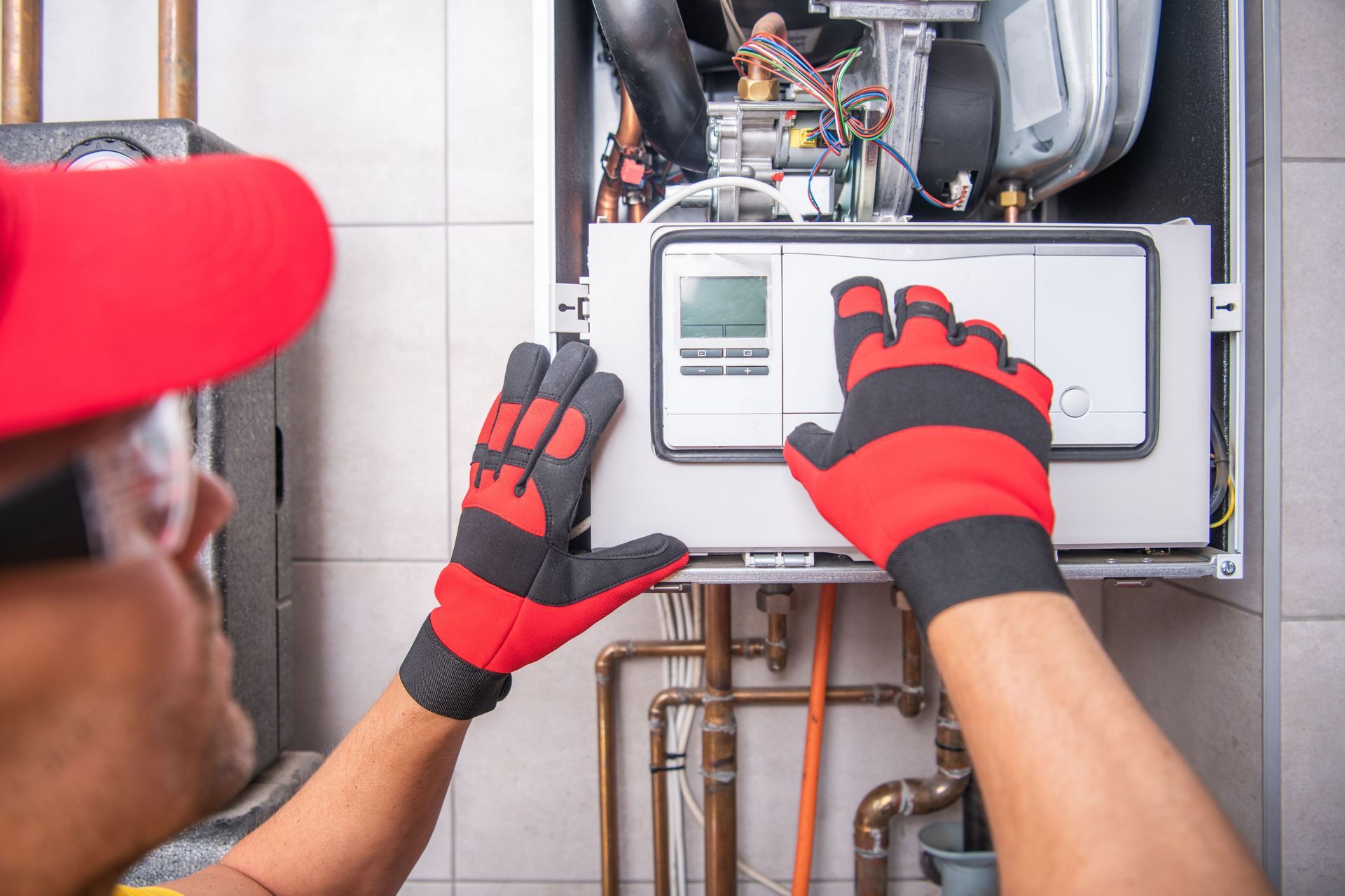 A man in a red hat and gloves is working on a boiler.