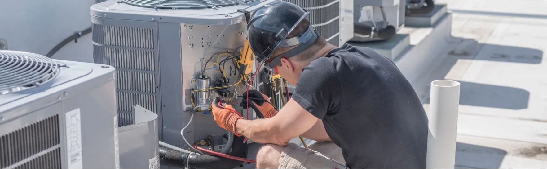 A man is working on an air conditioner on the roof of a building.