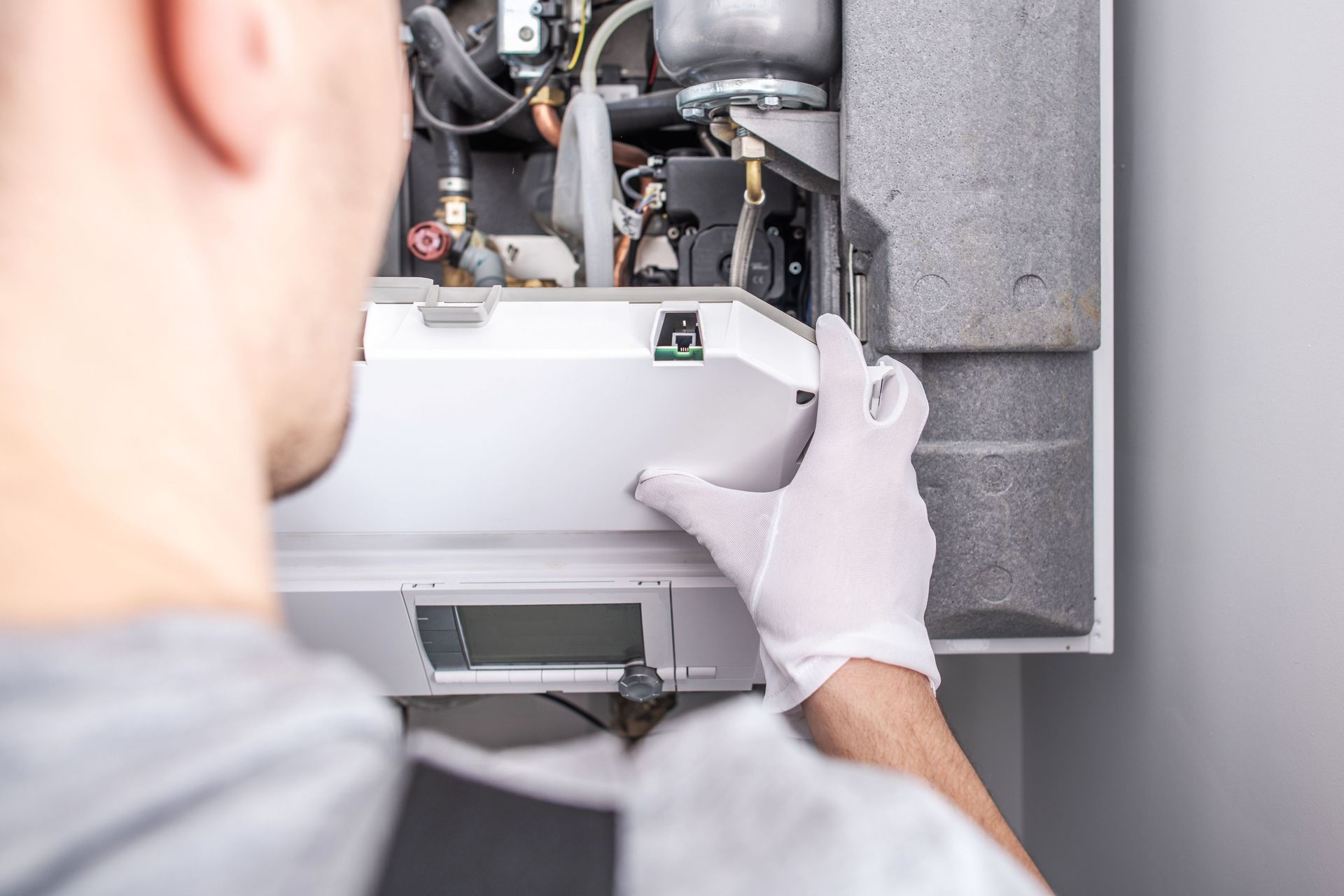 A man wearing white gloves is fixing a boiler.