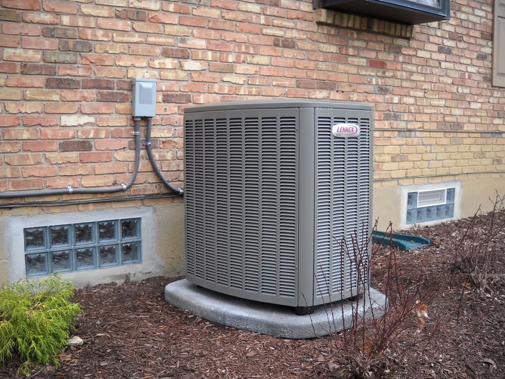 A large air conditioner is sitting on the side of a brick building.