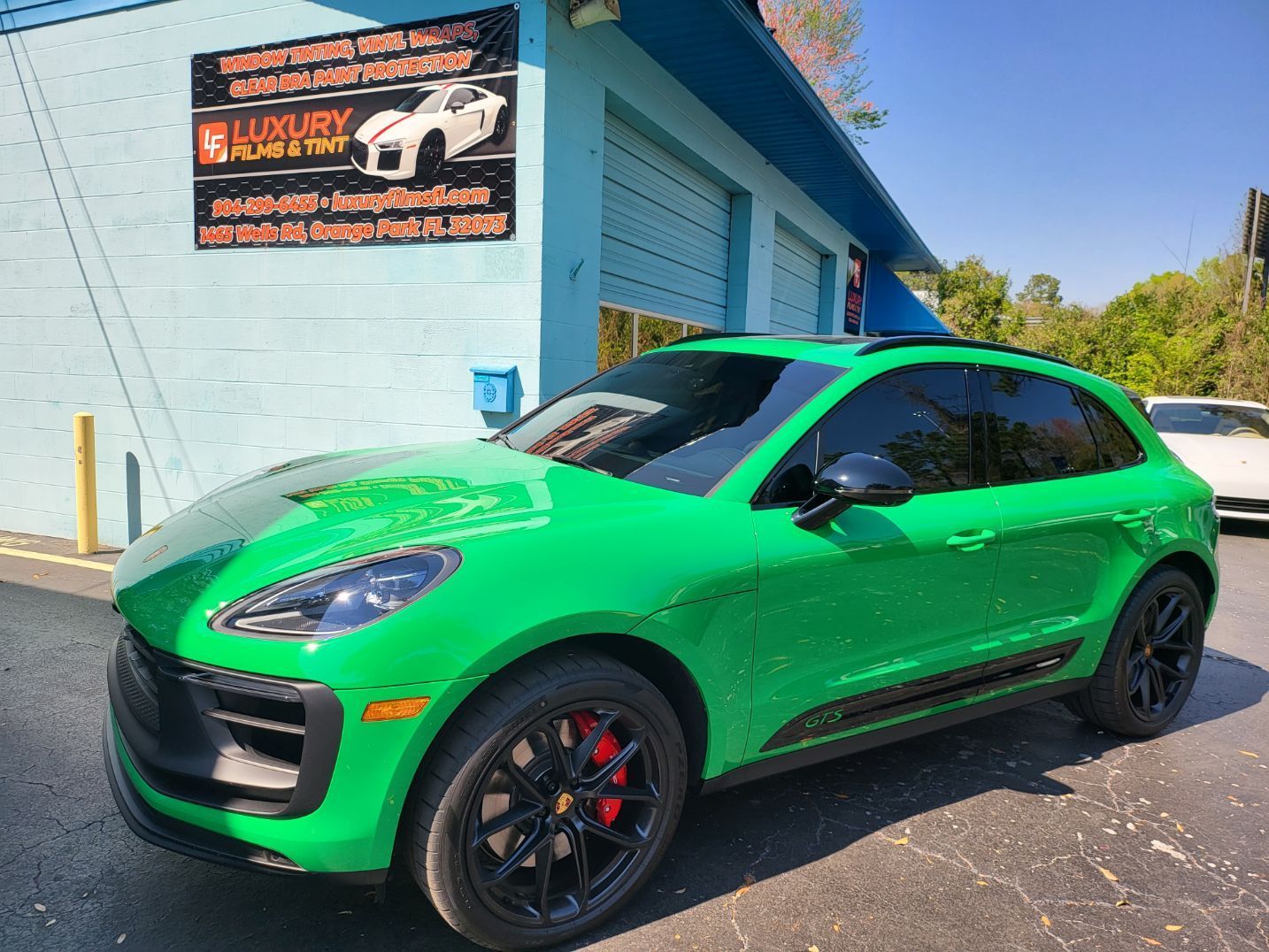 A green porsche macan gts is parked in front of a building.
