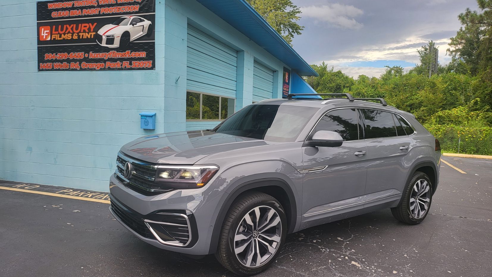 A gray volkswagen atlas is parked in front of a blue building.