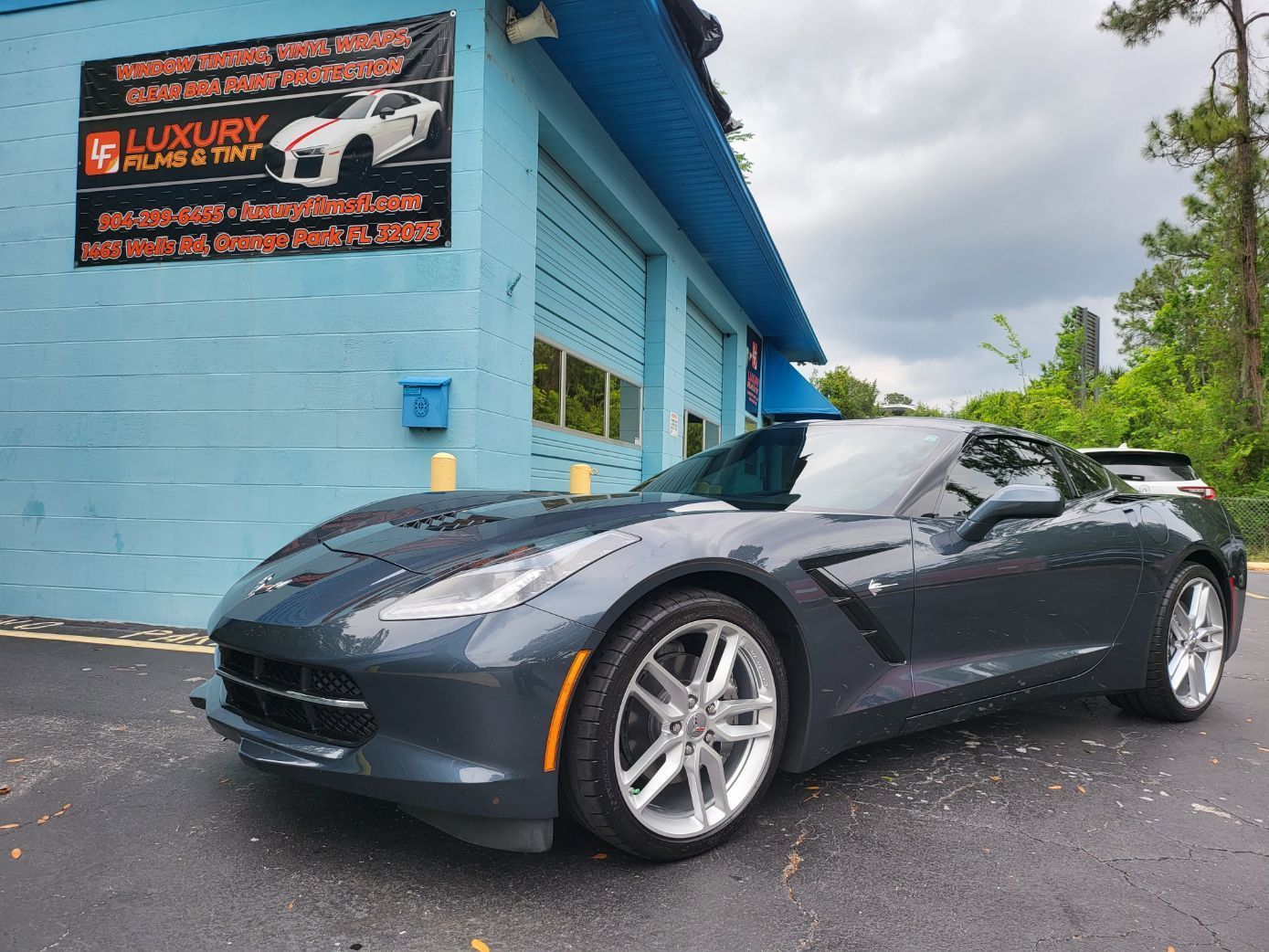 A gray sports car is parked in front of a luxury car dealership