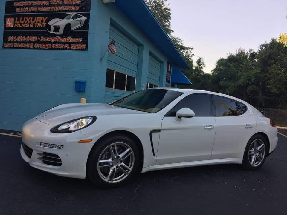 A white porsche panamera is parked in front of a building.