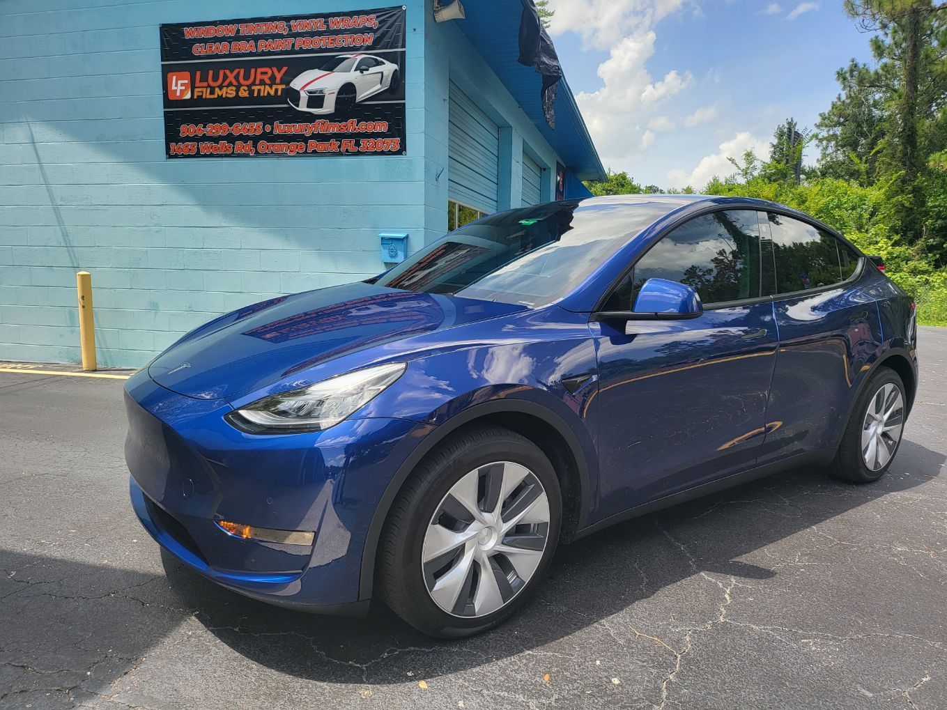 A blue tesla model y is parked in front of a building.