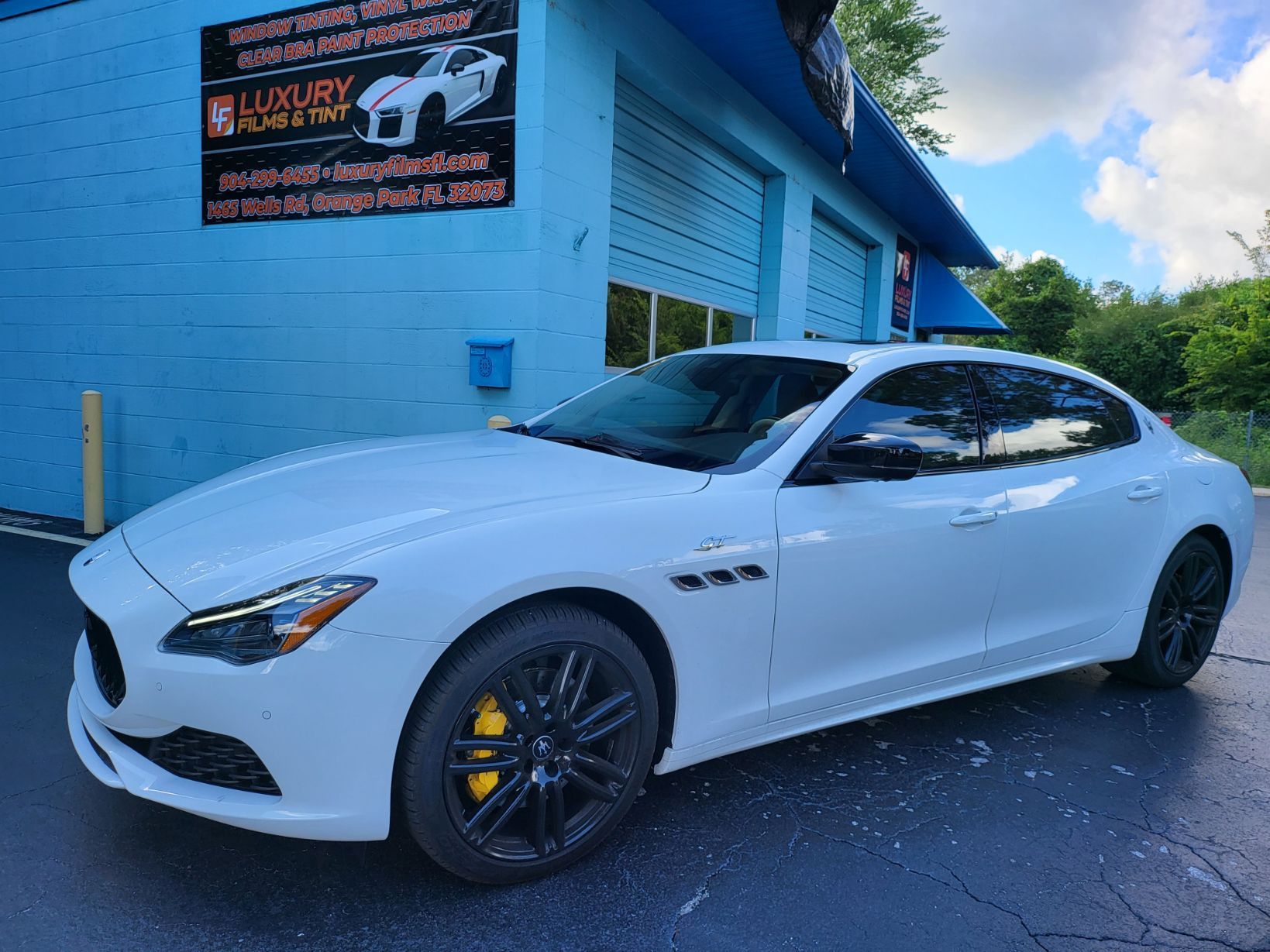 A white maserati is parked in front of a blue building.