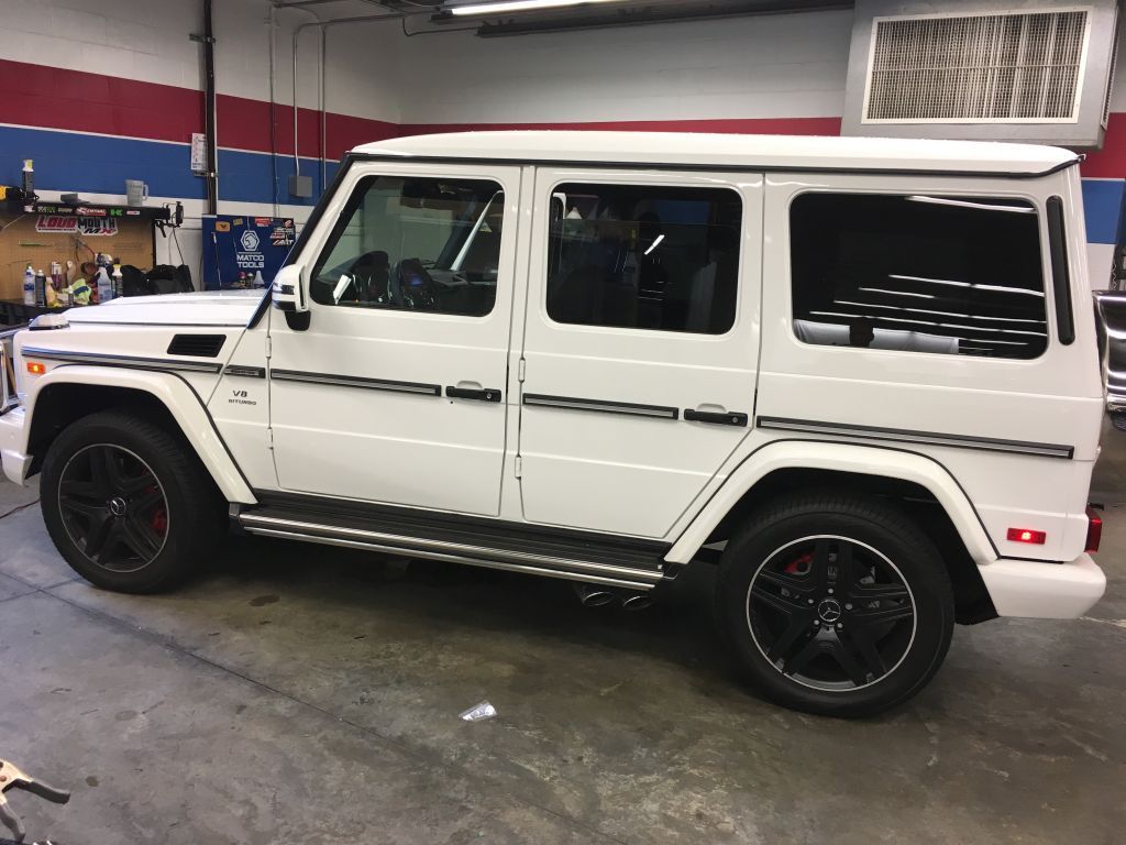 A white mercedes benz g63 is parked in a garage.