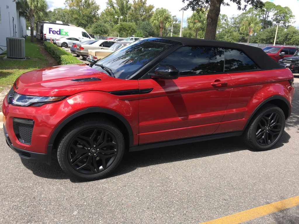 A red range rover evoque convertible is parked in a parking lot.