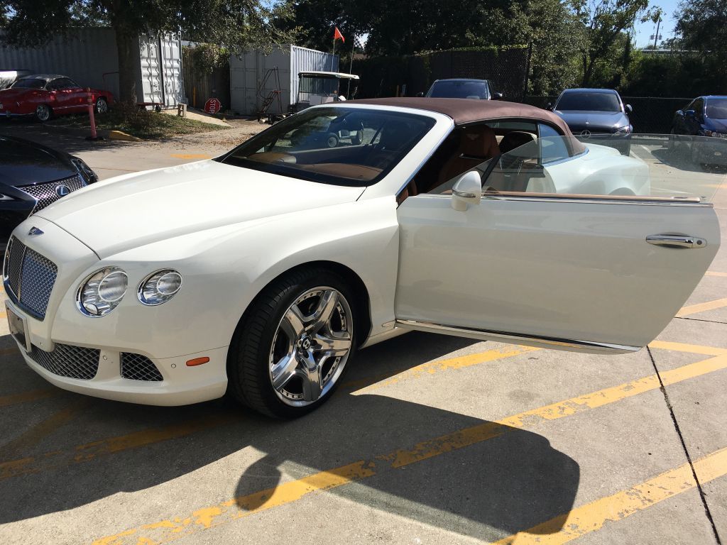 A white bentley convertible is parked in a parking lot with its doors open.