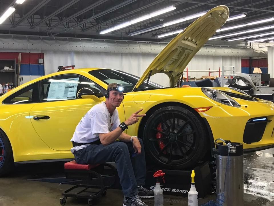 A man is sitting next to a yellow sports car with the hood up.