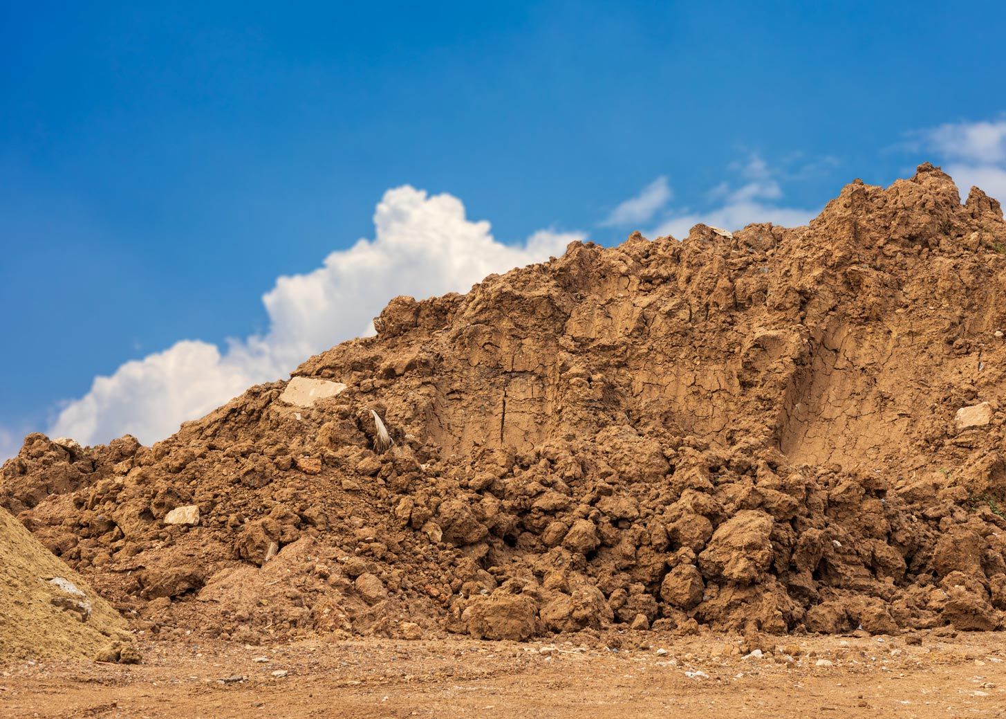 A large pile of dirt against a blue sky with clouds.