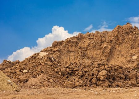 A large pile of dirt against a blue sky with clouds.