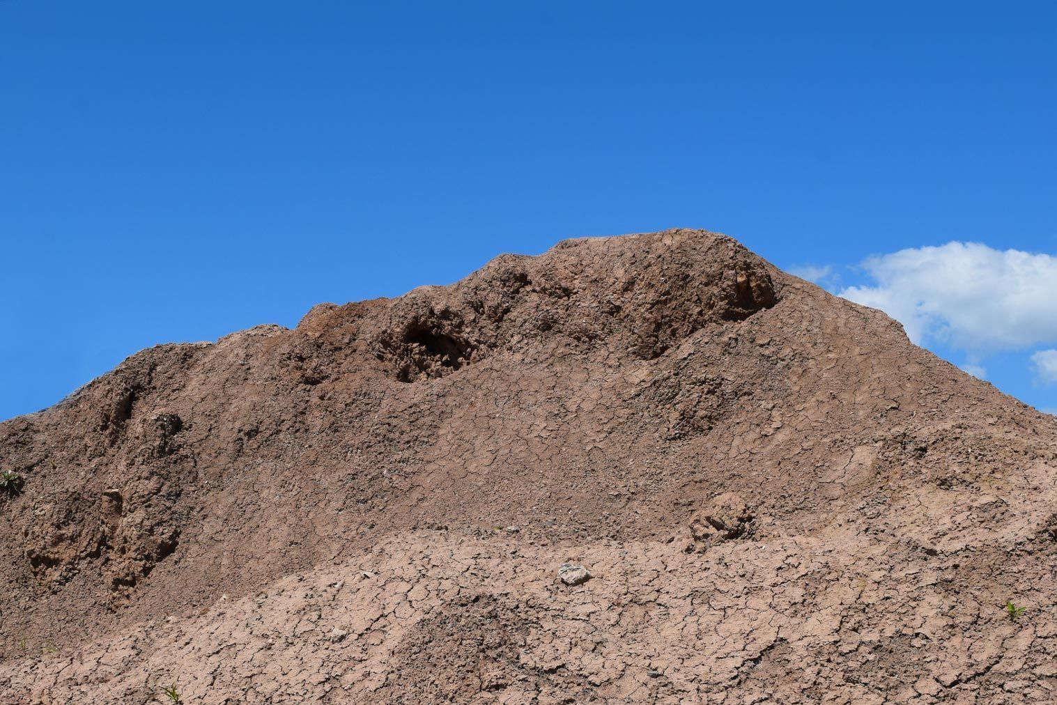 A large pile of dirt is against a blue sky.