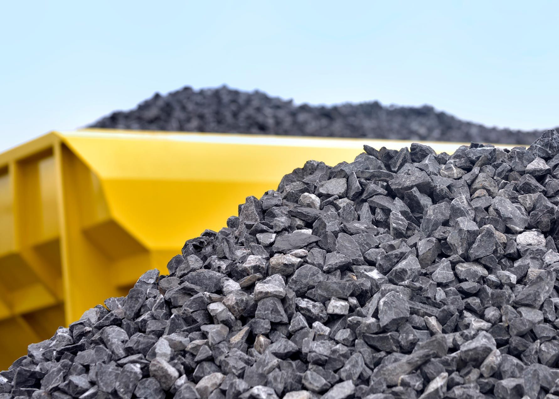 A pile of coal is sitting next to a yellow dumpster.