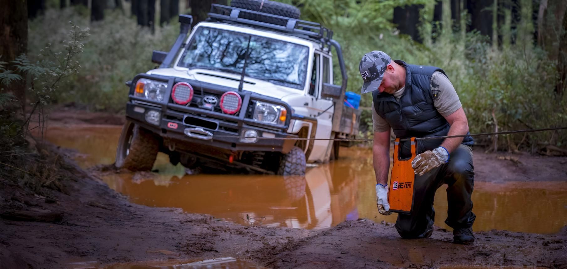 A Man Is Kneeling Next To A Jeep That Is Stuck In The Mud — Tech Tune Automotive and 4x4 ARB In Innisfail, QLD