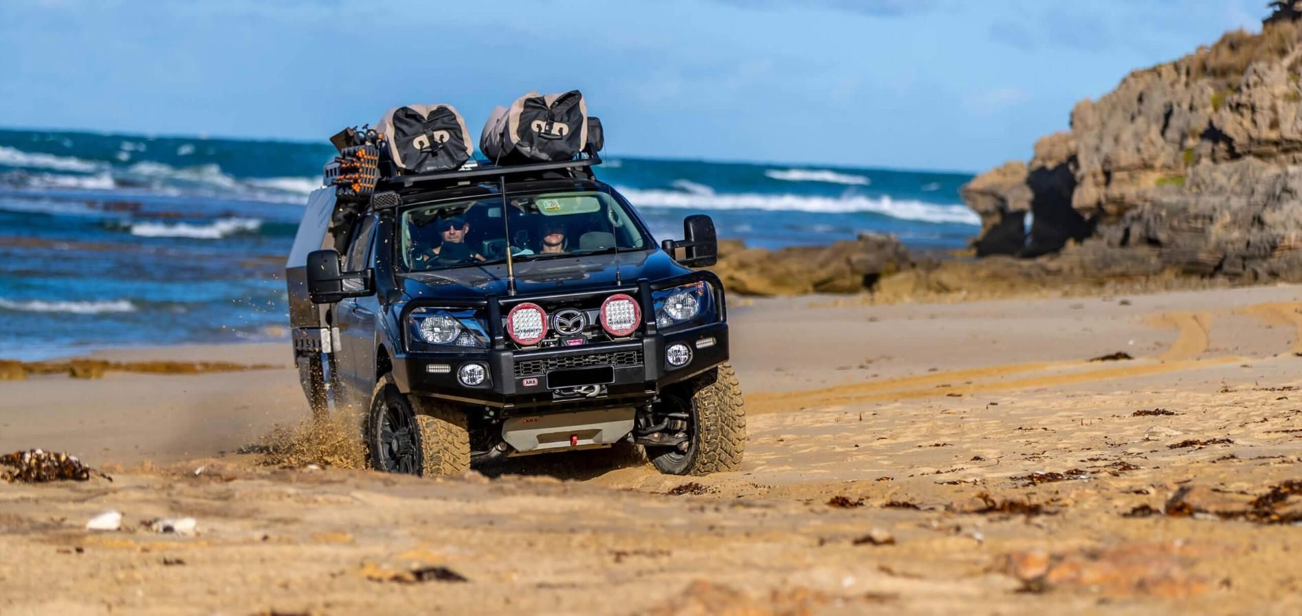 A Black Truck Is Driving On A Sandy Beach Near The Ocean — Tech Tune Automotive and 4x4 ARB In Babinda, QLD