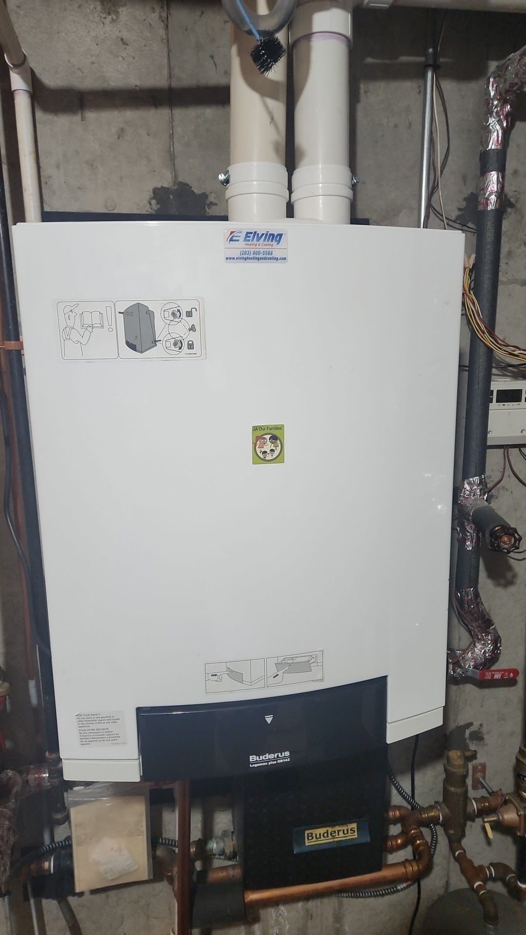 White wall-mounted boiler with black lower panel, copper pipes, white vents in a basement setting.