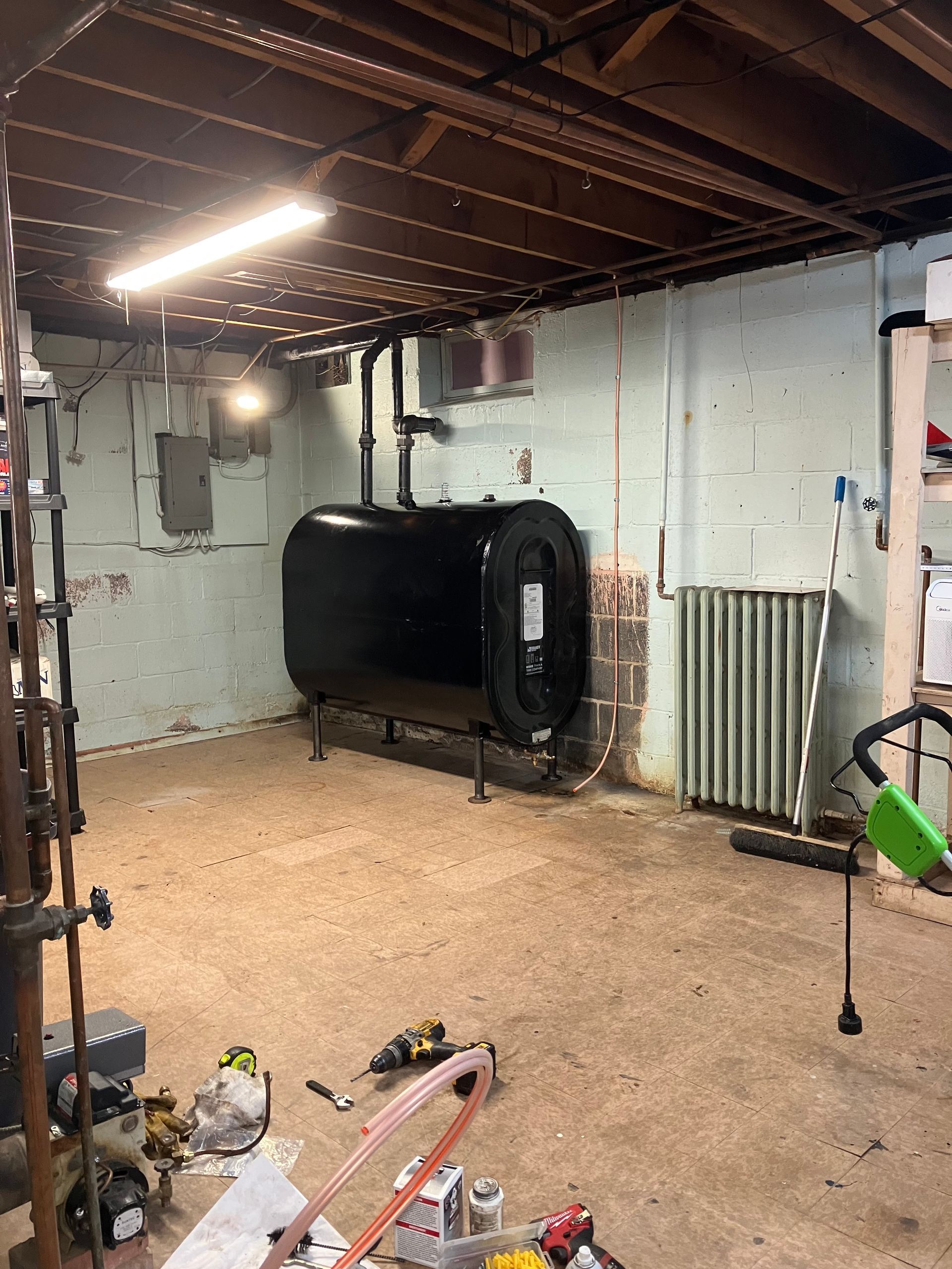 Basement with an oil tank, exposed ceiling beams, and various tools scattered on the floor.
