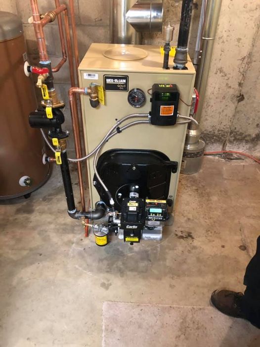 Oil-fired boiler in a basement, with copper pipes and a burner.
