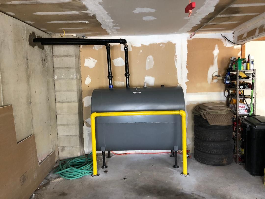 Oil tank in a garage with black pipes, yellow safety frame, and stacked tires.