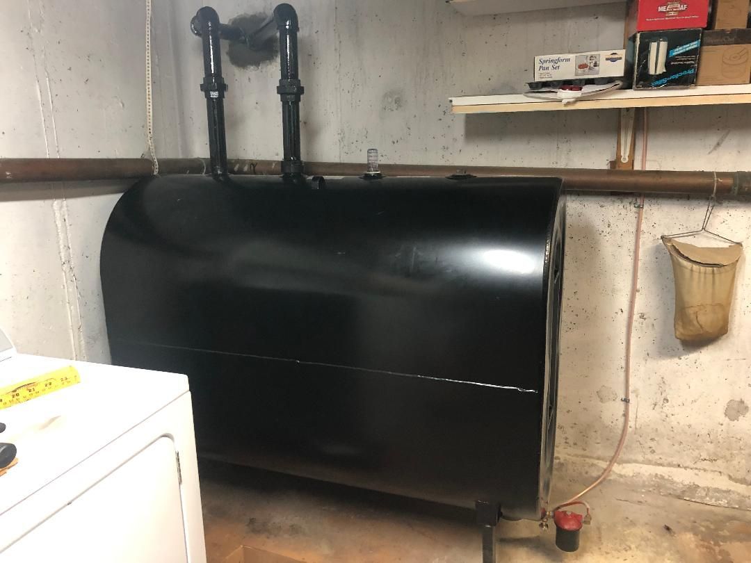 Black oil tank in a basement with copper pipes and a white wall.
