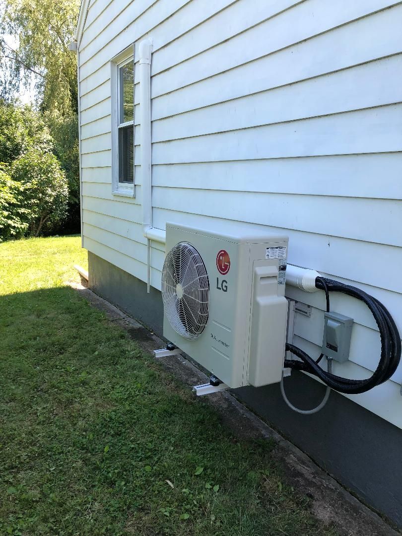 LG air conditioning unit mounted on a white house exterior. Black insulated tubing and electrical box visible.